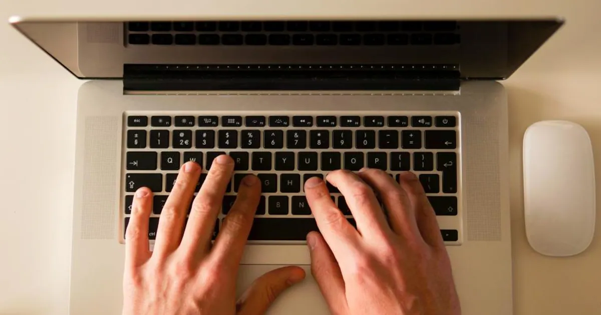 Manos escribiendo en el teclado de un portátil sobre una mesa de trabajo
