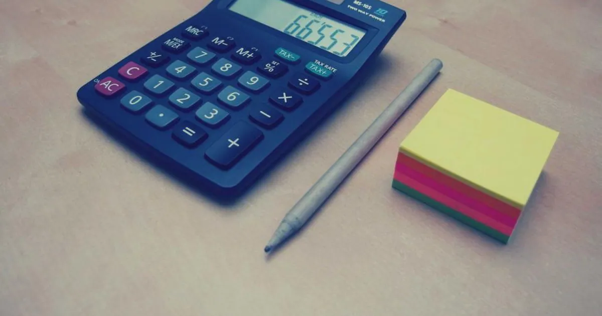 Calculadora, bolígrafo y un taco de notas de colores sobre una mesa de trabajo