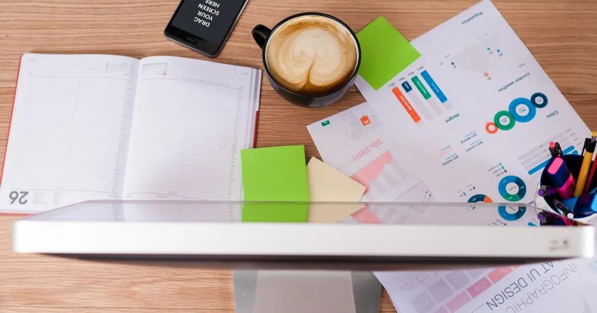 Escritorio con informes de gráficos y métricas impresos, una agenda abierta, una tablet y una taza de café